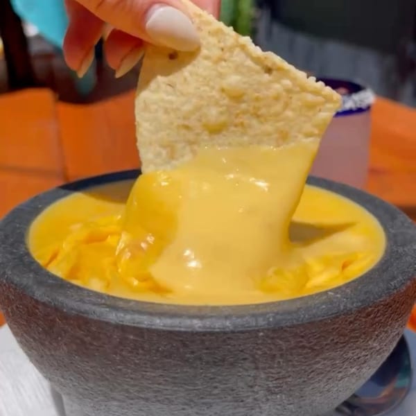 A hand dips a tortilla chip into a bowl of melted yellow queso at Uno Mas Taqueria y Cantina.