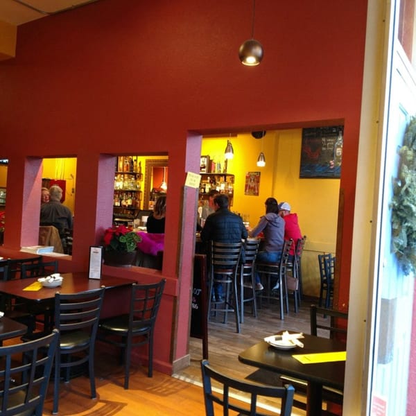 Restaurant interior with red walls, a bar area, and dining tables with black chairs.