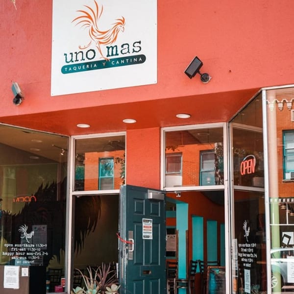 Exterior of Uno Mas Taqueria y Cantina with a red facade, open door, and visible signage.