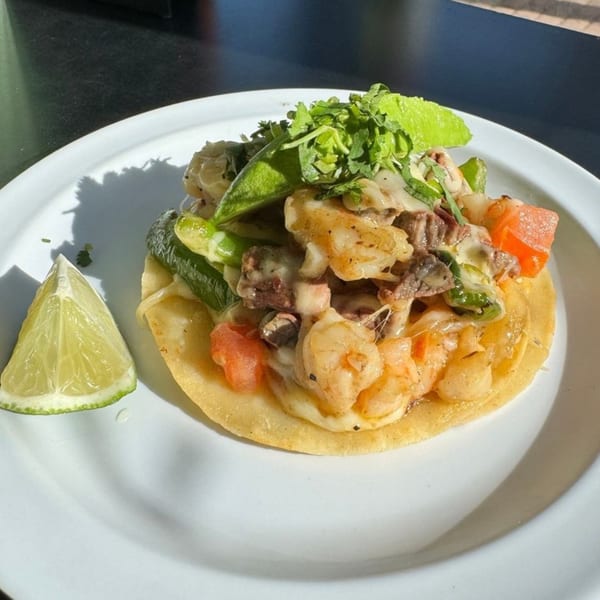 Uno Mas Taqueria y Cantina's shrimp and steak taco with melted cheese, peppers, and a lime wedge.