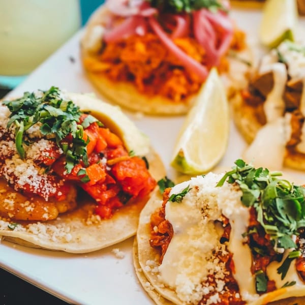 A close-up of several vibrant Uno Mas Taqueria y Cantina tacos with various toppings and a lime wedge.