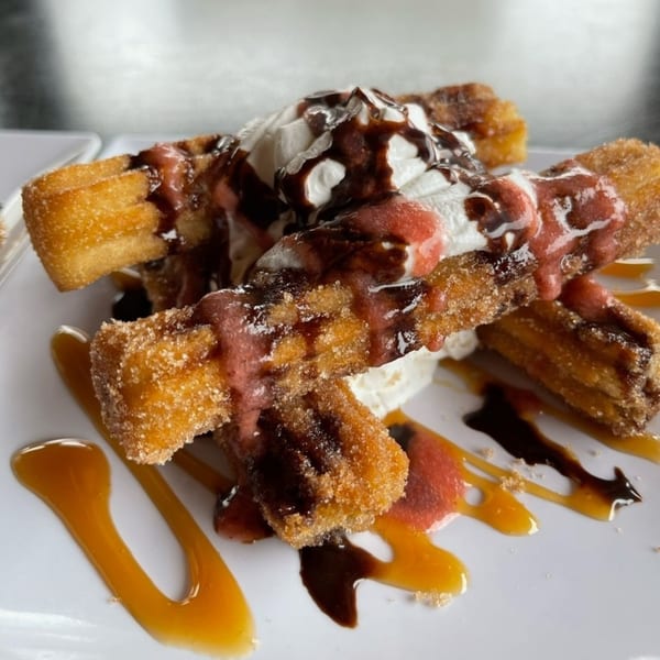 Churros with whipped cream, chocolate, and strawberry drizzle on a white plate at Uno Mas Taqueria y Cantina.
