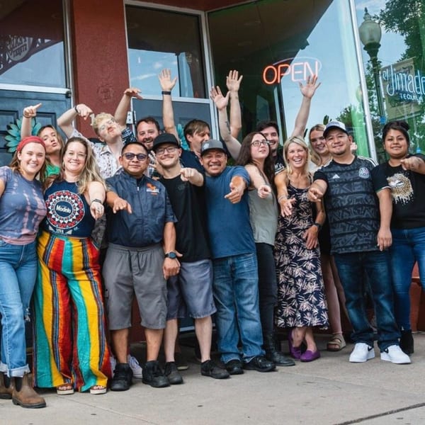 A large group of Uno Mas Taqueria y Cantina staff smiling and posing outside the restaurant.
