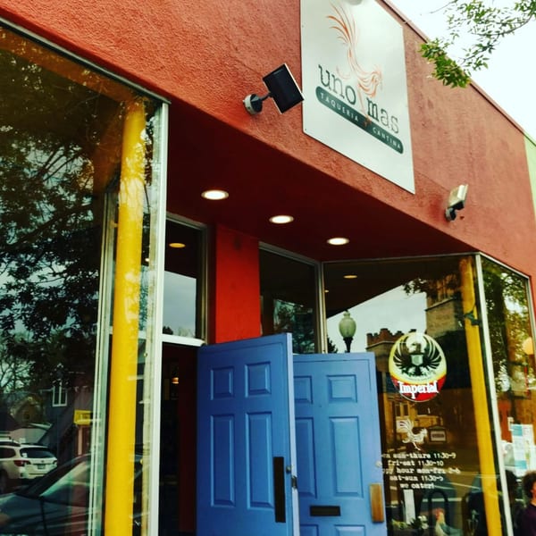 The vibrant red exterior of Uno Mas Taqueria y Cantina with open blue doors and large windows.